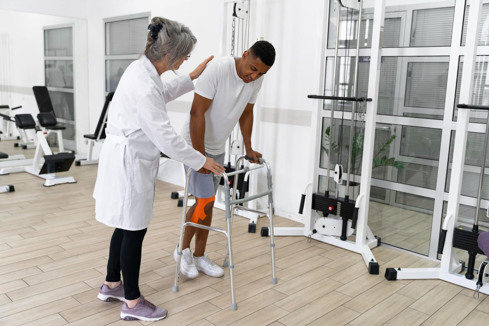Man using a walker under supervision during physical injury rehabilitation in a physiotherapy clinic