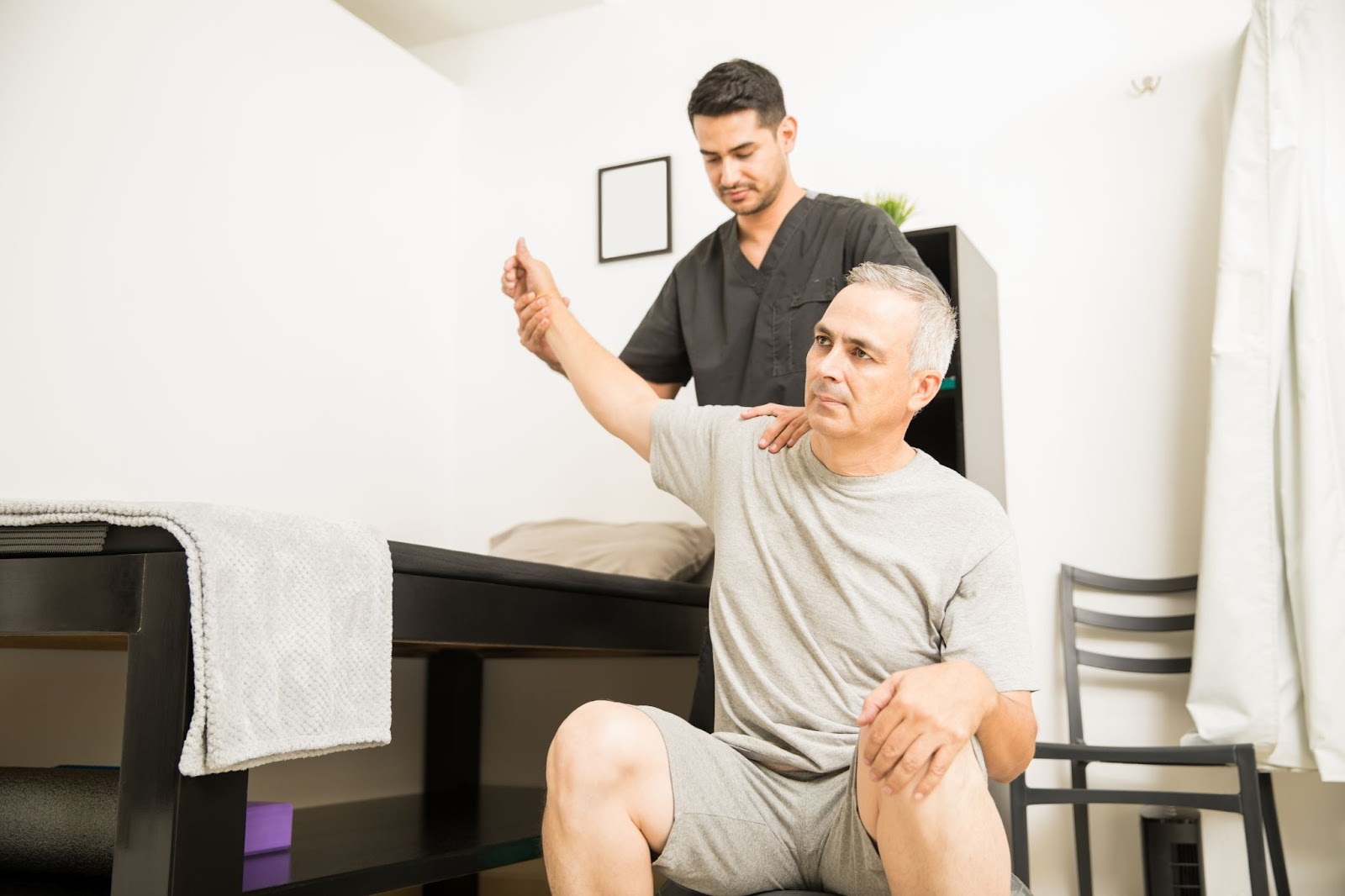 Physiotherapist performing manual therapy physiotherapy on a middle-aged man’s shoulder to improve mobility and reduce pain