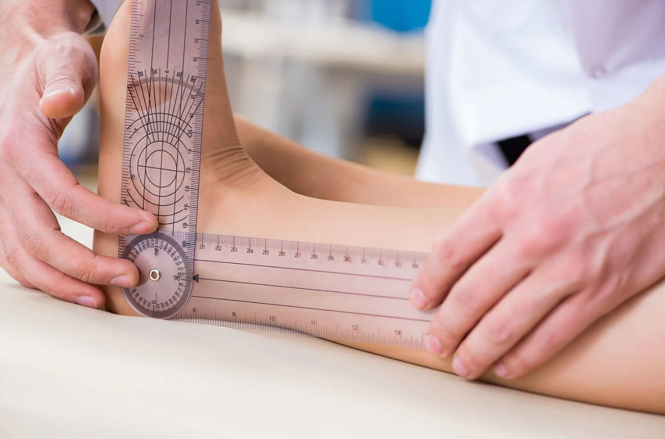 Podiatrist performing biomechanical assessment podiatry using a goniometer to measure ankle joint movement
